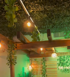 Luminárias pendentes acesas entre vigas de madeira e vegetação decorativa